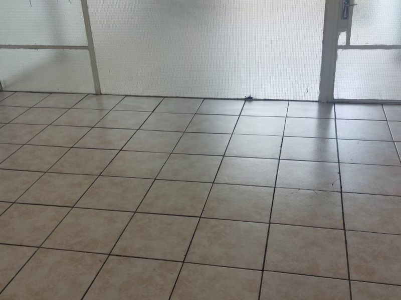 An empty living area featuring neutral floor tiles and a security screen door, providing a blank canvas for potential interior updates.