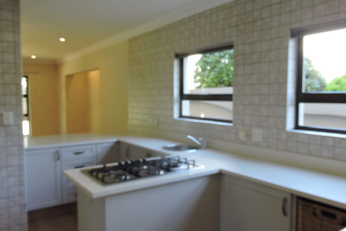 A functional kitchen featuring built-in cabinetry, a gas hob, and tiled splashbacks, offering a clean and neutral space ready for personalization.