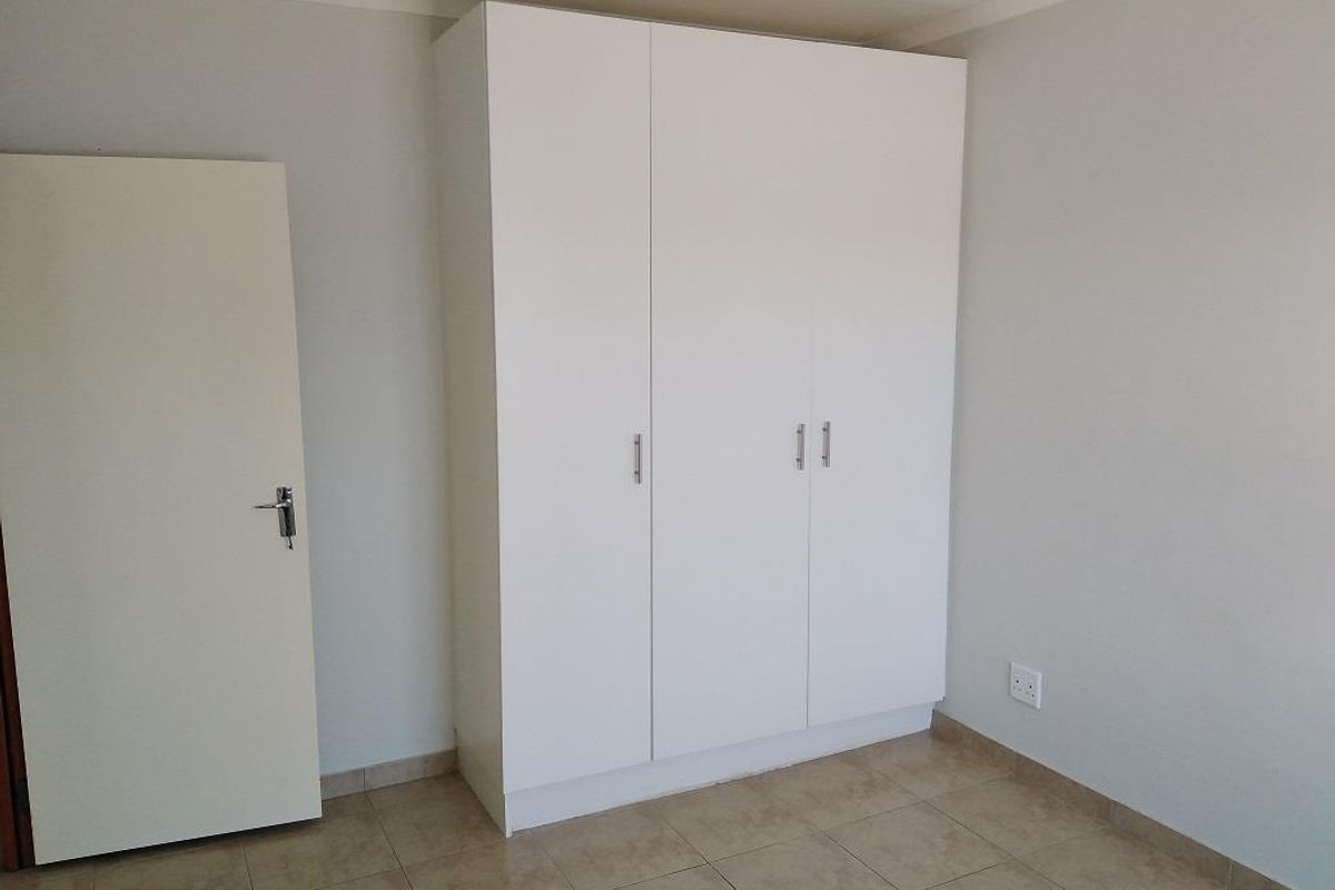 A clean, empty bedroom featuring neutral tiled flooring and a modern white built-in wardrobe.