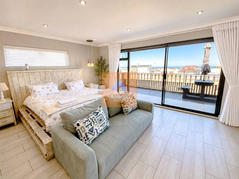 Spacious bedroom featuring modern tiled flooring, recessed lighting, and large sliding glass doors opening onto a private balcony with coastal views.