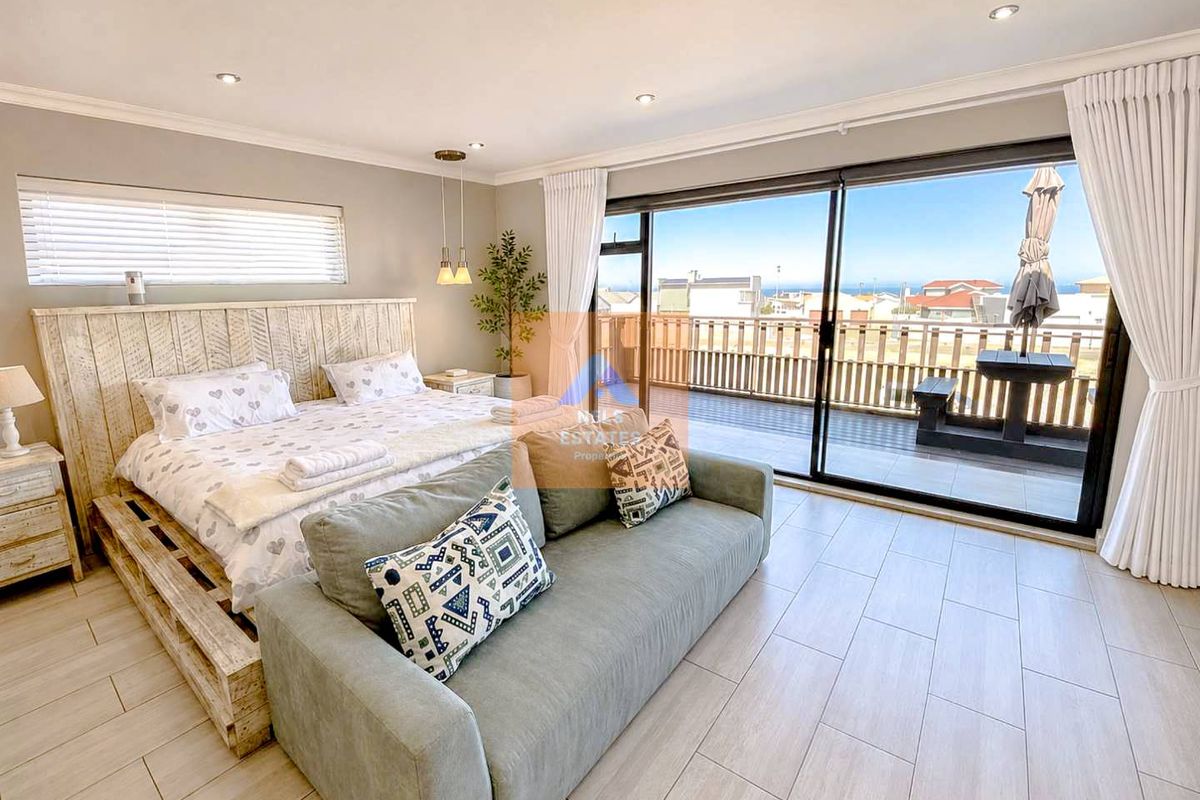 Spacious bedroom featuring modern tiled flooring, recessed lighting, and large sliding glass doors opening onto a private balcony with coastal views.