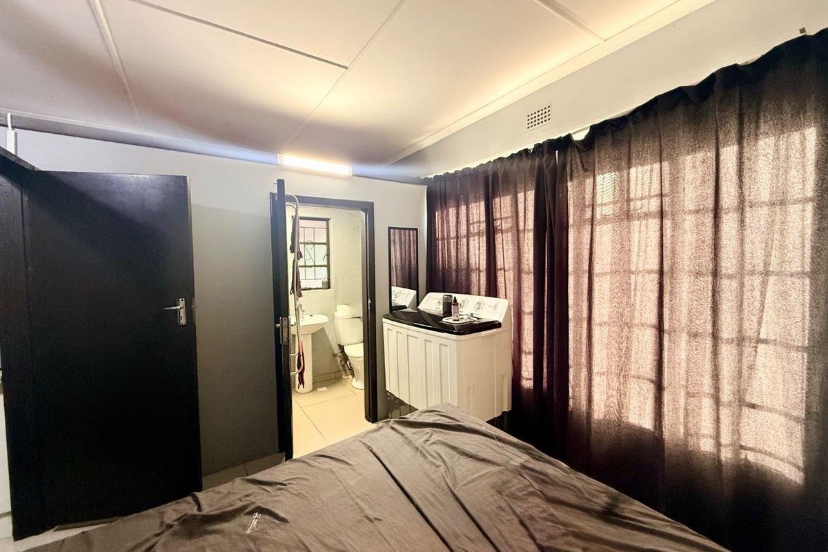 A bedroom featuring an en-suite bathroom and integrated laundry area, with large windows and neutral wall finishes.