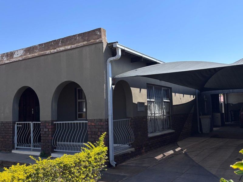 Front elevation of a single-story house featuring an arched porch, brick detailing, and a large shade cloth carport over the driveway.