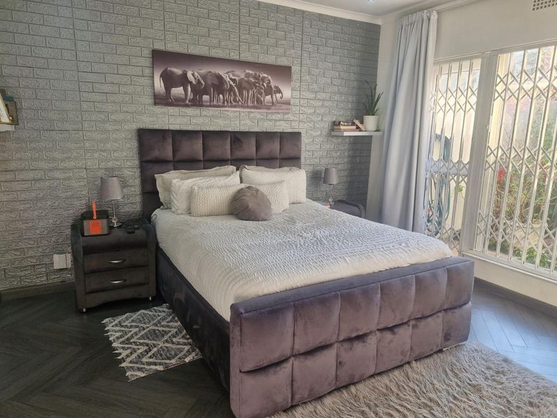 A well-maintained bedroom featuring herringbone flooring, a textured faux brick accent wall, and direct access to the exterior through a secure sliding door.