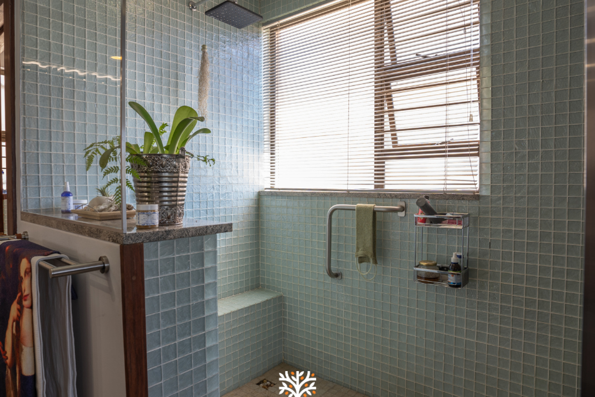 A well-maintained bathroom shower area featuring light blue mosaic wall tiles, a built-in shower bench, a rainfall showerhead, and a window with fitted blinds.