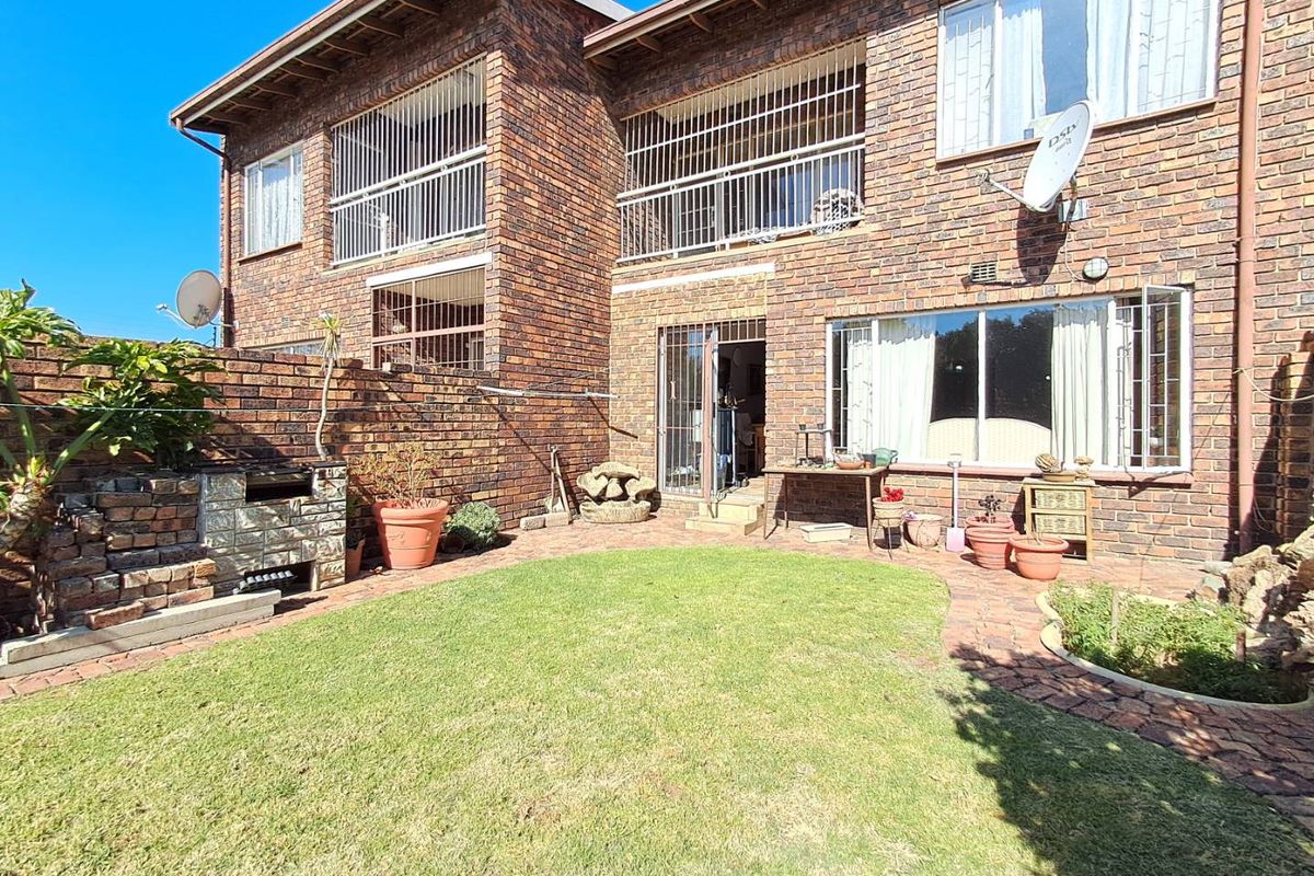 Rear view of a townhouse featuring a private garden, paved patio area, built-in brick braai, and upper-level balconies with security bars.