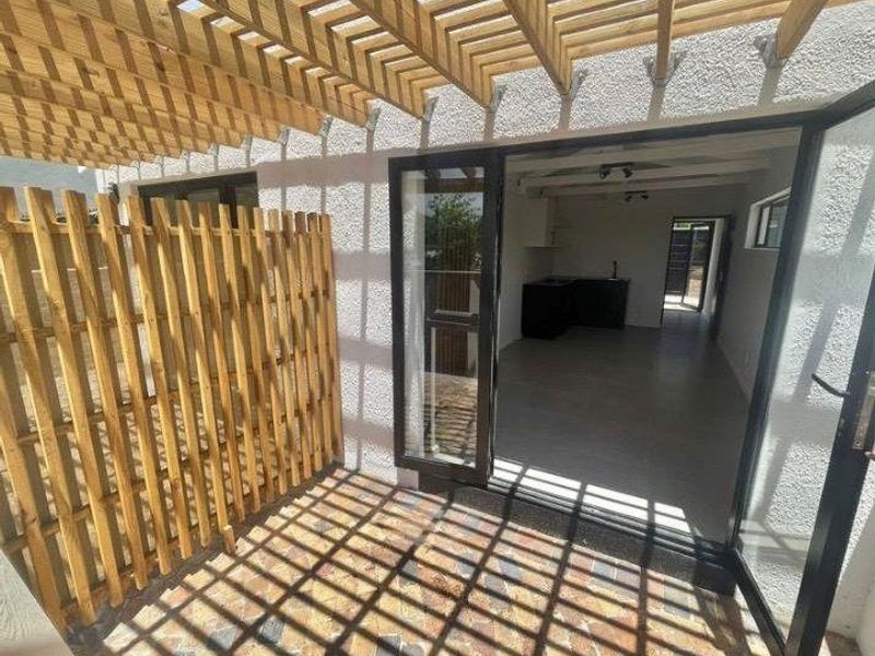 A private patio area featuring a wooden pergola, privacy screen, and bi-fold glass doors leading into the apartment interior.