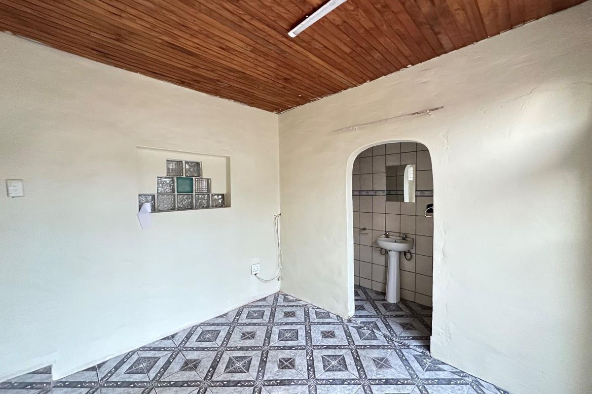 A small interior room featuring a timber-clad ceiling, patterned floor tiles, a glass block feature wall, and an arched doorway leading to a small bathroom.