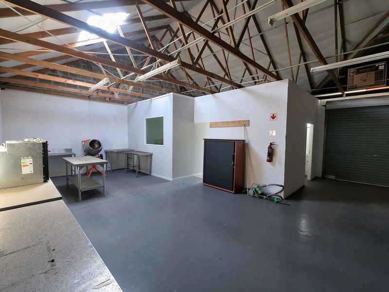 Spacious industrial utility area featuring exposed timber roof trusses, durable epoxy flooring, roller shutter access, and painted masonry walls.