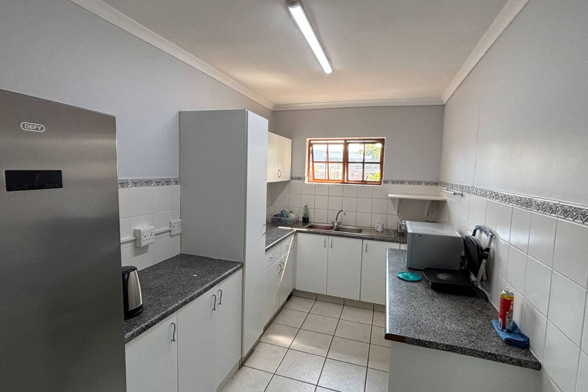 A functional office kitchen featuring white cabinetry, granite-look countertops, tiled splashbacks, and a stainless steel sink.