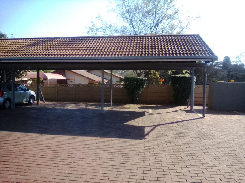 A covered carport area featuring a tiled roof structure and paved driveway, situated within a secure complex with precast boundary walling.