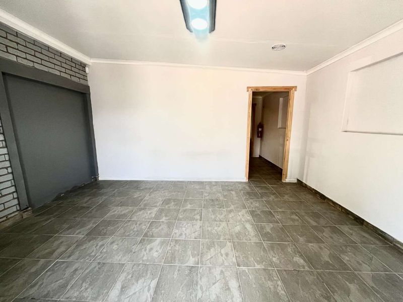 An empty living area featuring grey tiled flooring, an exposed brick accent wall, and a doorway leading to an adjacent space.