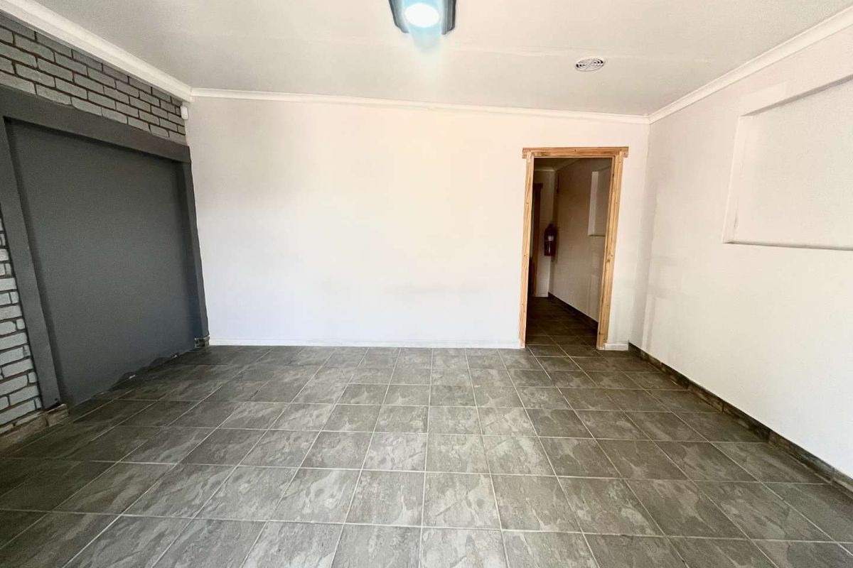 An empty living area featuring grey tiled flooring, an exposed brick accent wall, and a doorway leading to an adjacent space.