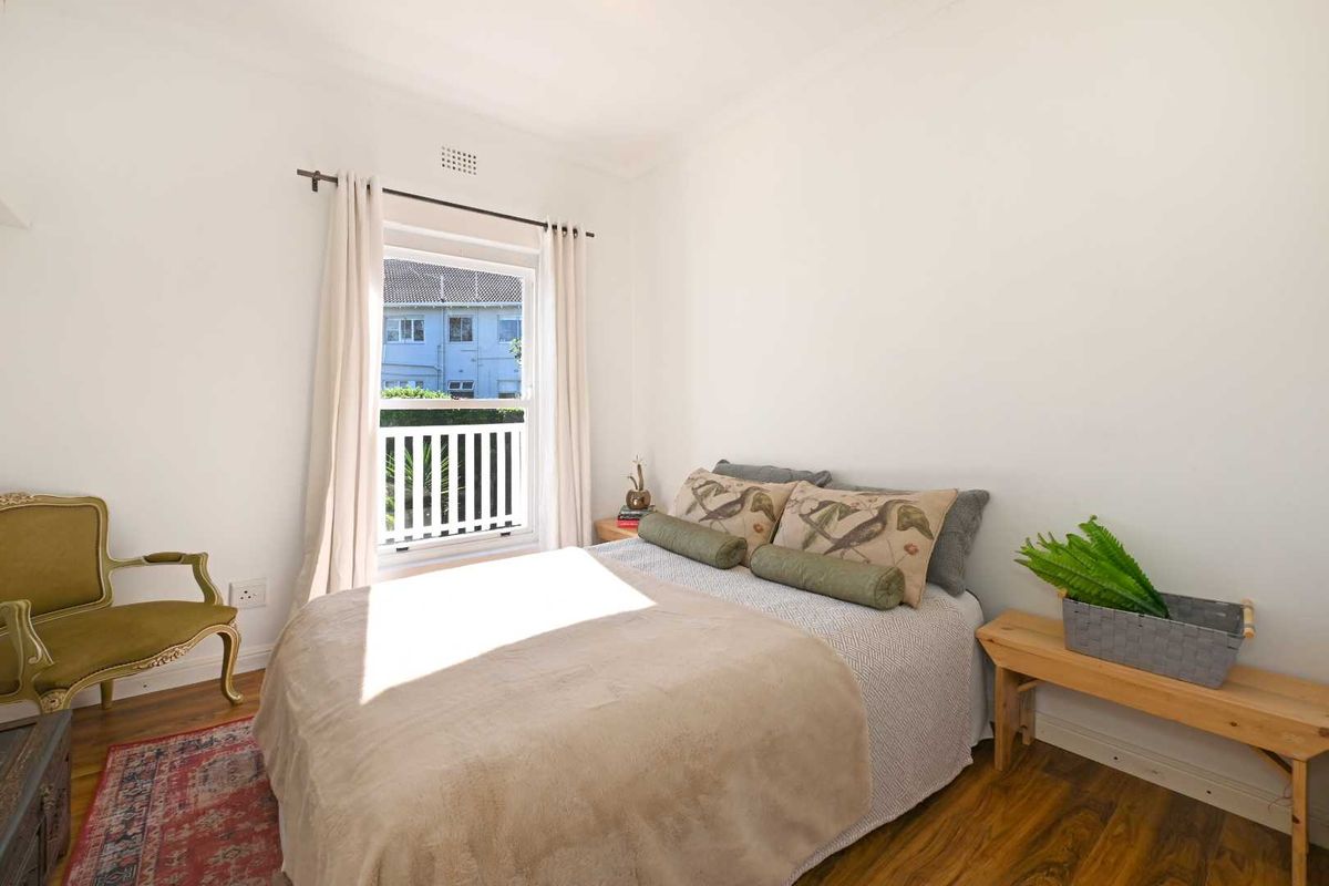 A bright and well-maintained bedroom featuring timber flooring, a sash window with a security railing, and neutral wall finishes.
