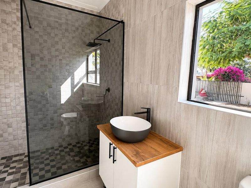 Modern bathroom featuring a walk-in shower with black frame, vessel sink on a wooden vanity, and contemporary tiled finishes.