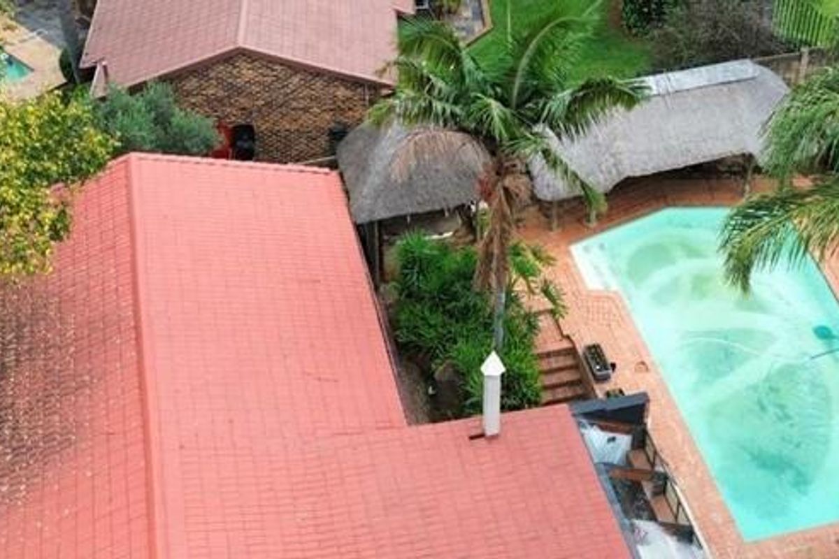 Aerial view of the property featuring a swimming pool, thatched lapa area, and red tiled roof structure set within a landscaped garden.