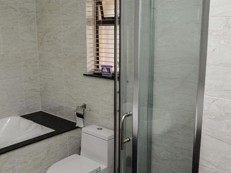 A modern bathroom featuring a glass-enclosed shower, a built-in bathtub, and a toilet, finished with neutral marble-look wall tiles and floor tiling.