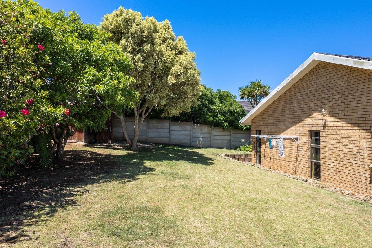 A private rear garden featuring a lawn area, mature trees, and a brick exterior wall with a mounted clothesline.