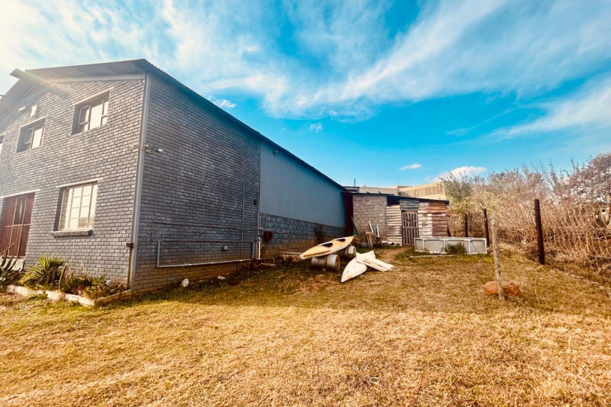 Rear view of the commercial property showing brick building facade, adjacent storage shed, and surrounding open land area.