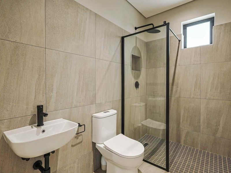 Modern bathroom featuring large format wall tiles, a walk-in shower with black-framed glass screen, matte black fixtures, and a wall-mounted basin.