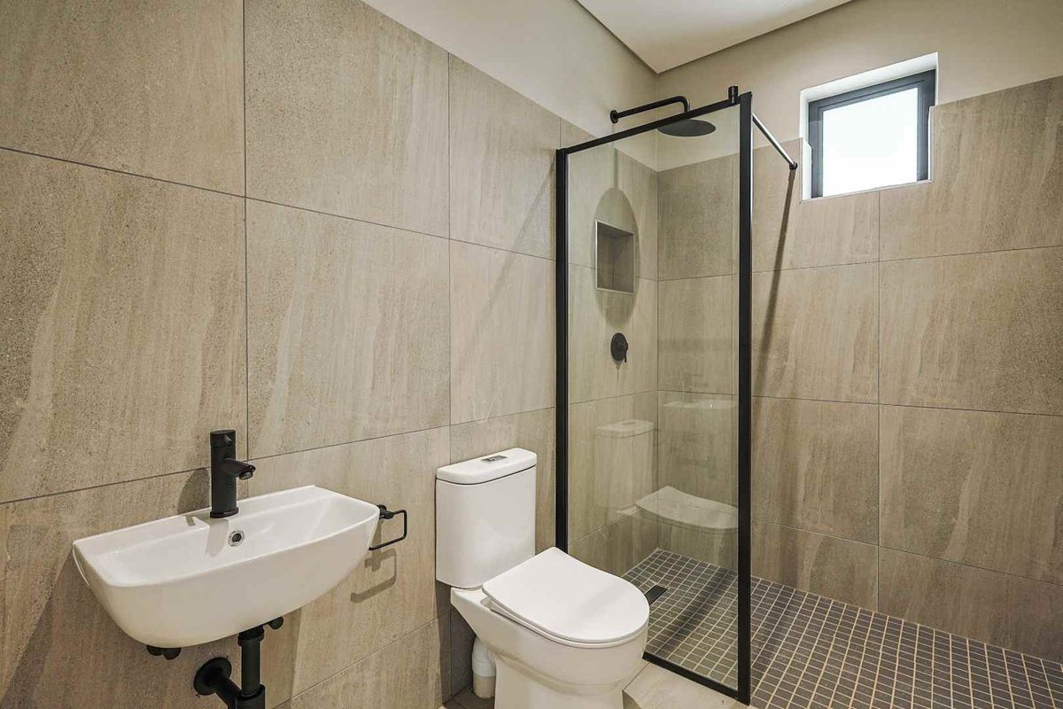 Modern bathroom featuring large format wall tiles, a walk-in shower with black-framed glass screen, matte black fixtures, and a wall-mounted basin.