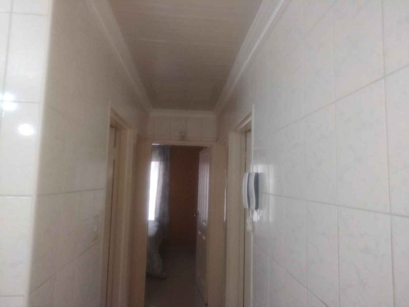 A narrow hallway featuring tiled walls and a coved ceiling, providing access to adjacent rooms within the property.