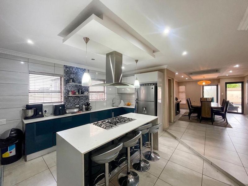 Modern open-plan kitchen and dining area featuring a central island with gas cooktop, sleek cabinetry, stone countertops, and contemporary recessed ceiling lighting.