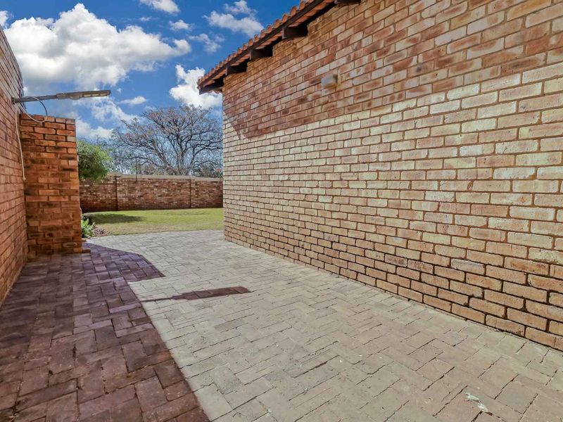 A side view of the townhouse showing a paved walkway, face brick exterior walls, and a view towards the rear garden area.
