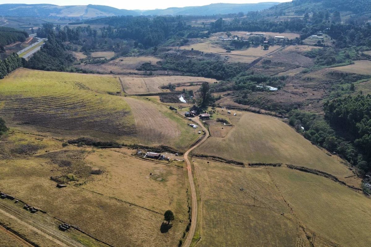 An aerial view of a large farm property featuring rolling hills, open grazing land, and a central dirt access road.