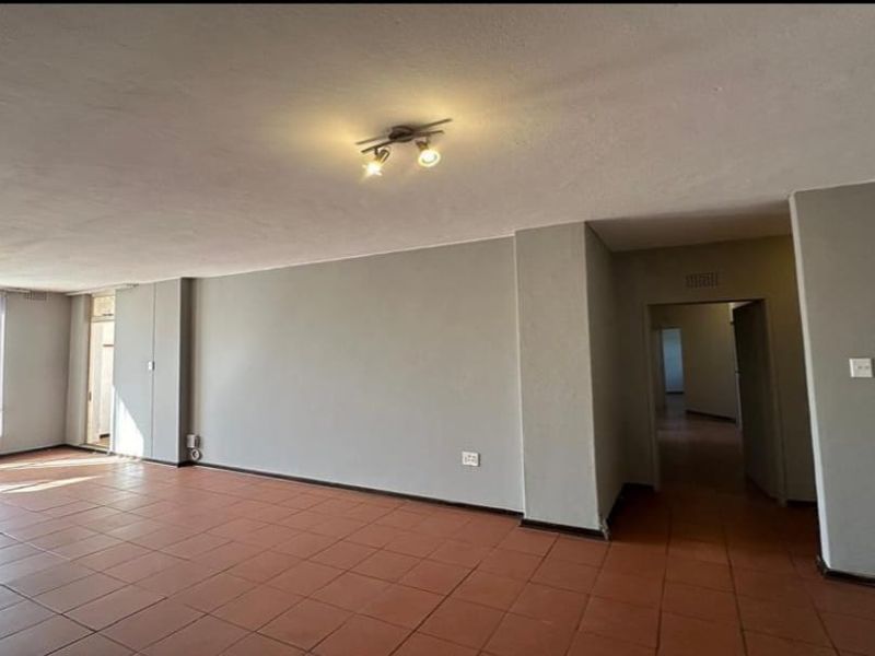 A spacious, empty living area featuring neutral grey walls, tiled flooring, and natural light from a large window.