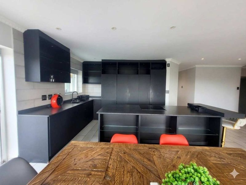 Modern kitchen featuring sleek black cabinetry, a central island with an integrated hob, and a tiled backsplash, offering a contemporary and functional cooking space.