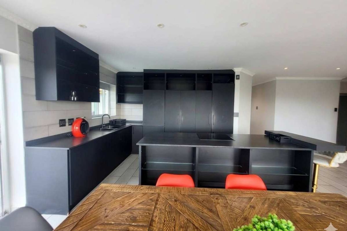 Modern kitchen featuring sleek black cabinetry, a central island with an integrated hob, and a tiled backsplash, offering a contemporary and functional cooking space.
