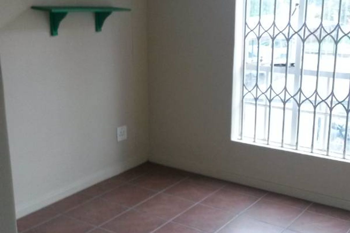 An empty bedroom featuring tiled flooring and a window fitted with security bars.