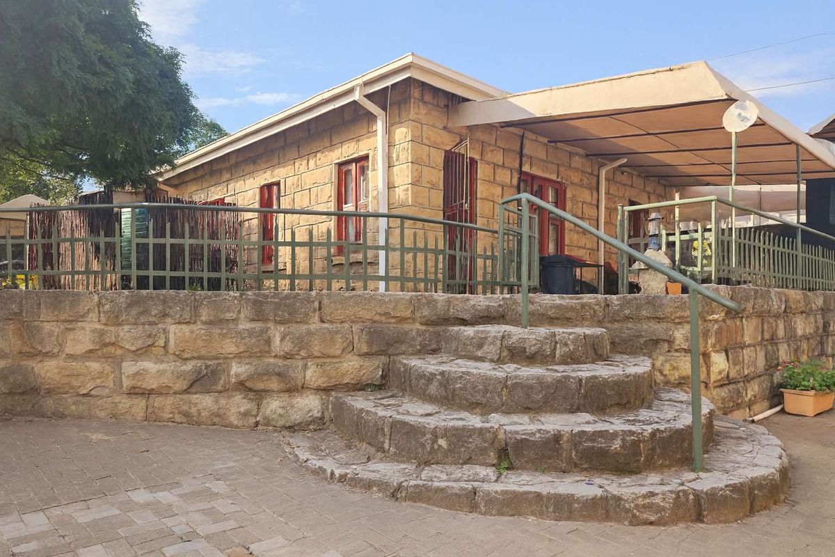 Exterior view of a stone-clad house featuring a raised patio area, stone steps, and a covered outdoor space with metal railings.
