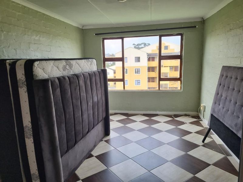 A bedroom featuring checkered tile flooring, painted brick walls, and a large window providing natural light and an urban view.