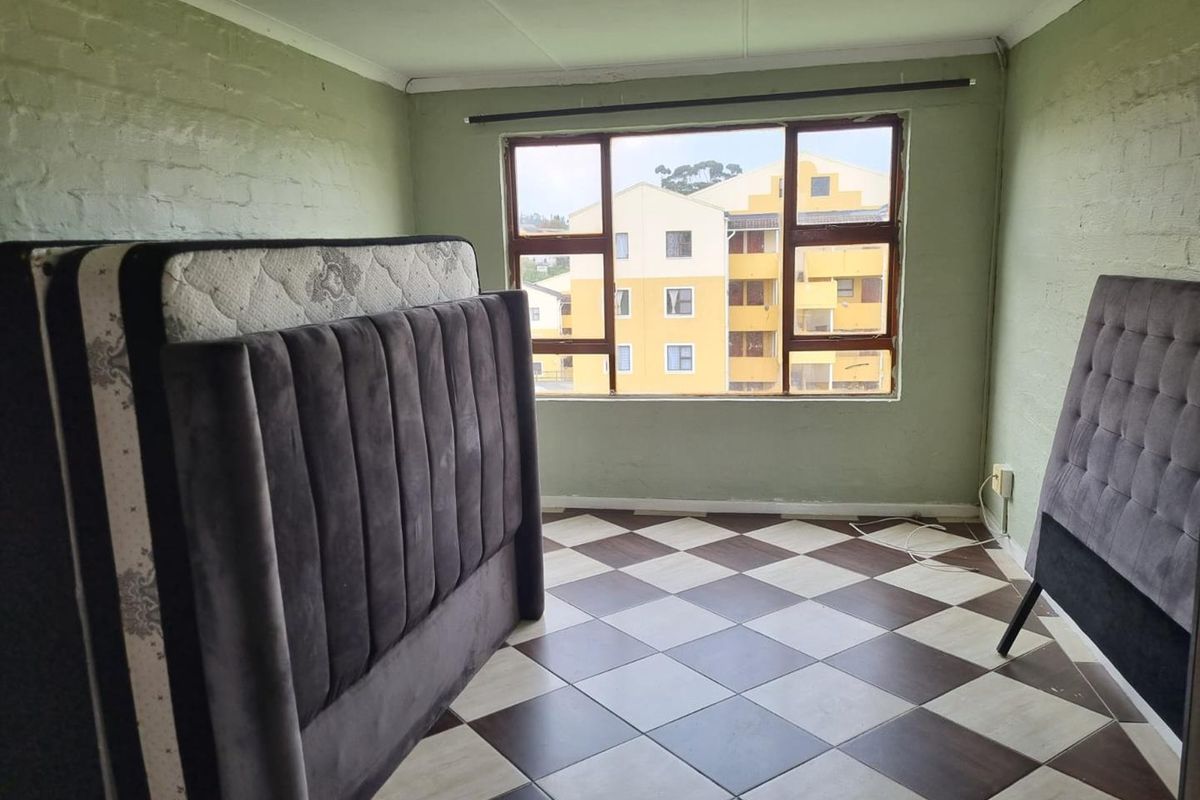 A bedroom featuring checkered tile flooring, painted brick walls, and a large window providing natural light and an urban view.