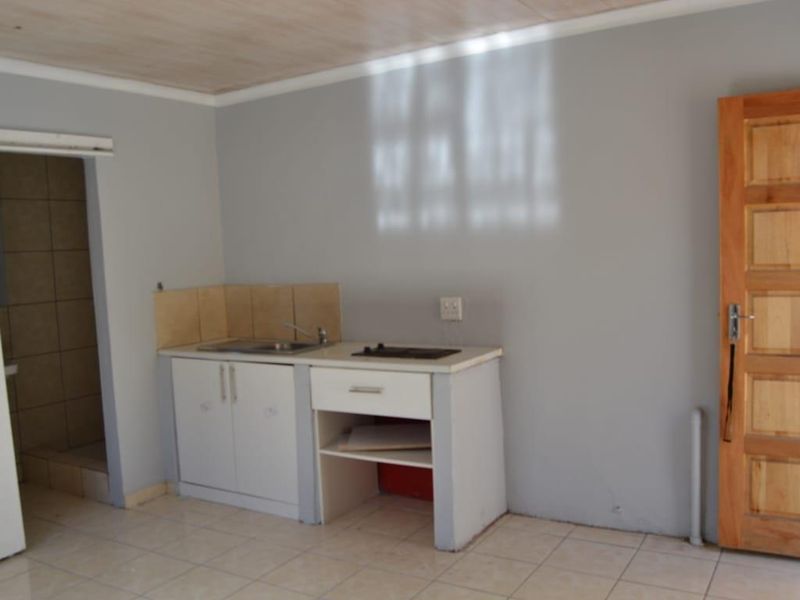 A compact kitchenette featuring basic cabinetry, a sink, and a built-in hob, set within a simple, tiled interior space.