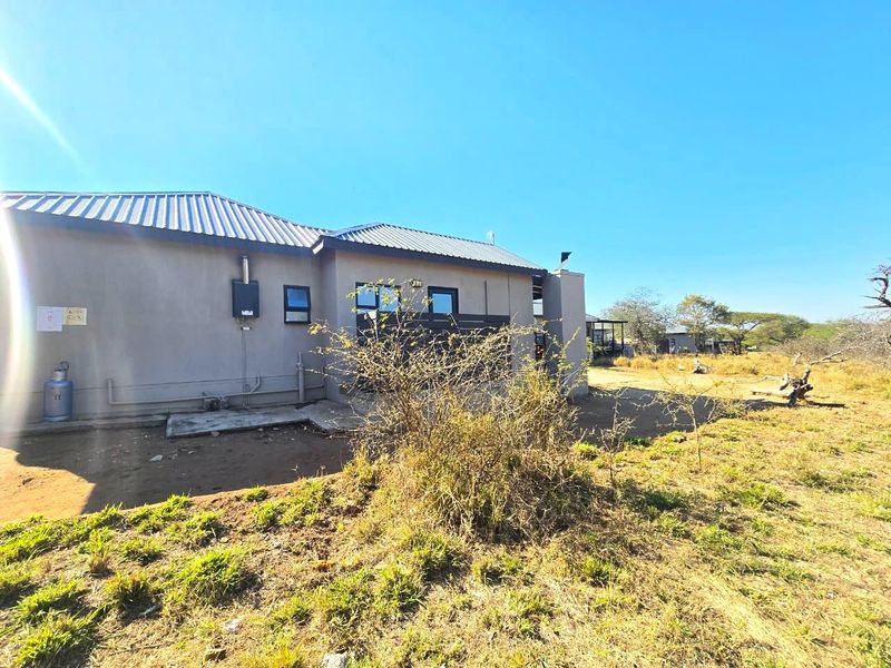 Rear view of the property showing the exterior wall, metal roofing, and installed gas geyser unit with surrounding natural landscape.