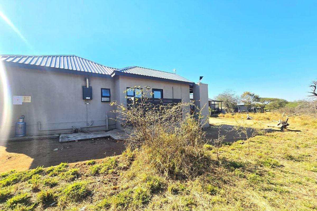 Rear view of the property showing the exterior wall, metal roofing, and installed gas geyser unit with surrounding natural landscape.