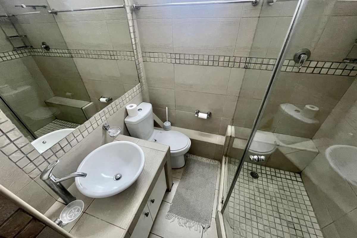 A compact bathroom featuring a glass-enclosed shower, a vanity with a vessel sink, and neutral wall tiling.