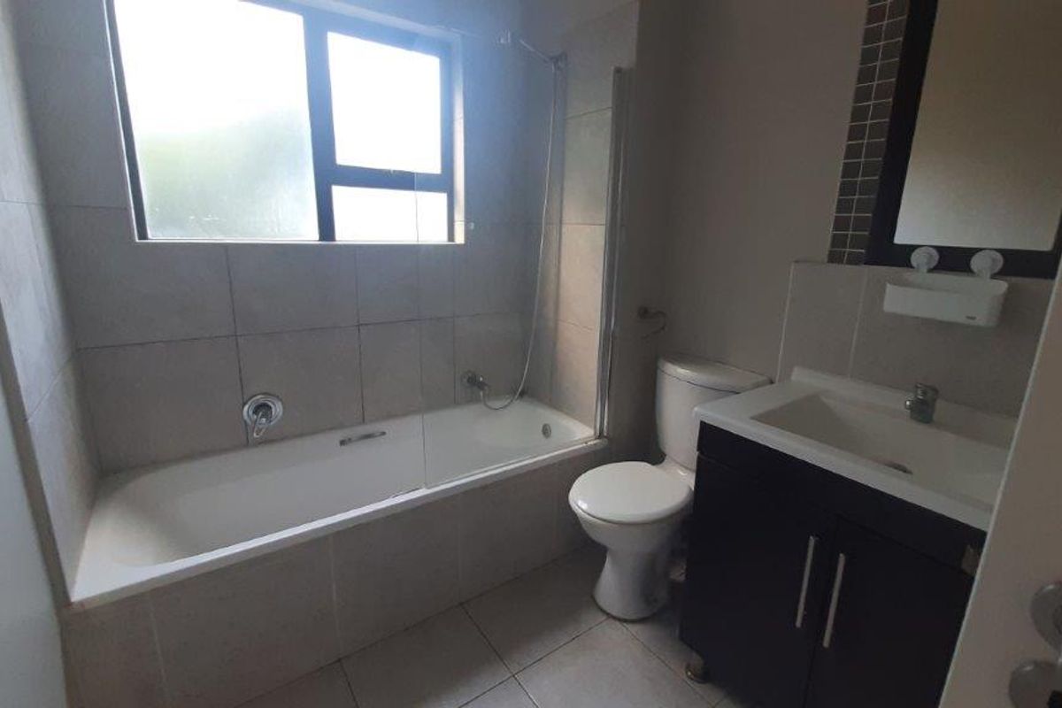 A functional bathroom featuring a built-in bathtub with shower mixer, a toilet, and a vanity cabinet with a basin.
