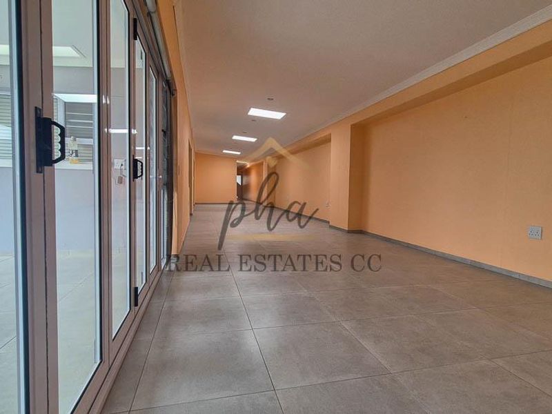 A spacious, empty living area featuring large aluminium stacker doors that open to the exterior, tiled flooring, and modern recessed downlighting.