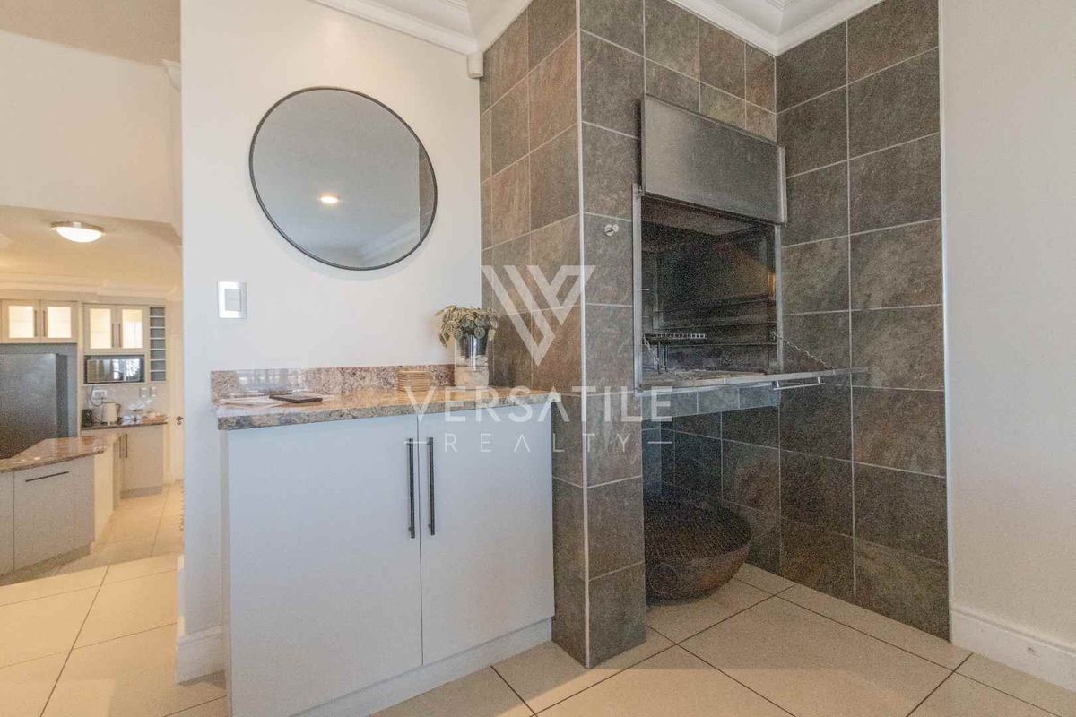 Indoor built-in braai area featuring tiled surround, granite countertop, and integrated cabinetry, adjacent to an open-plan kitchen space.