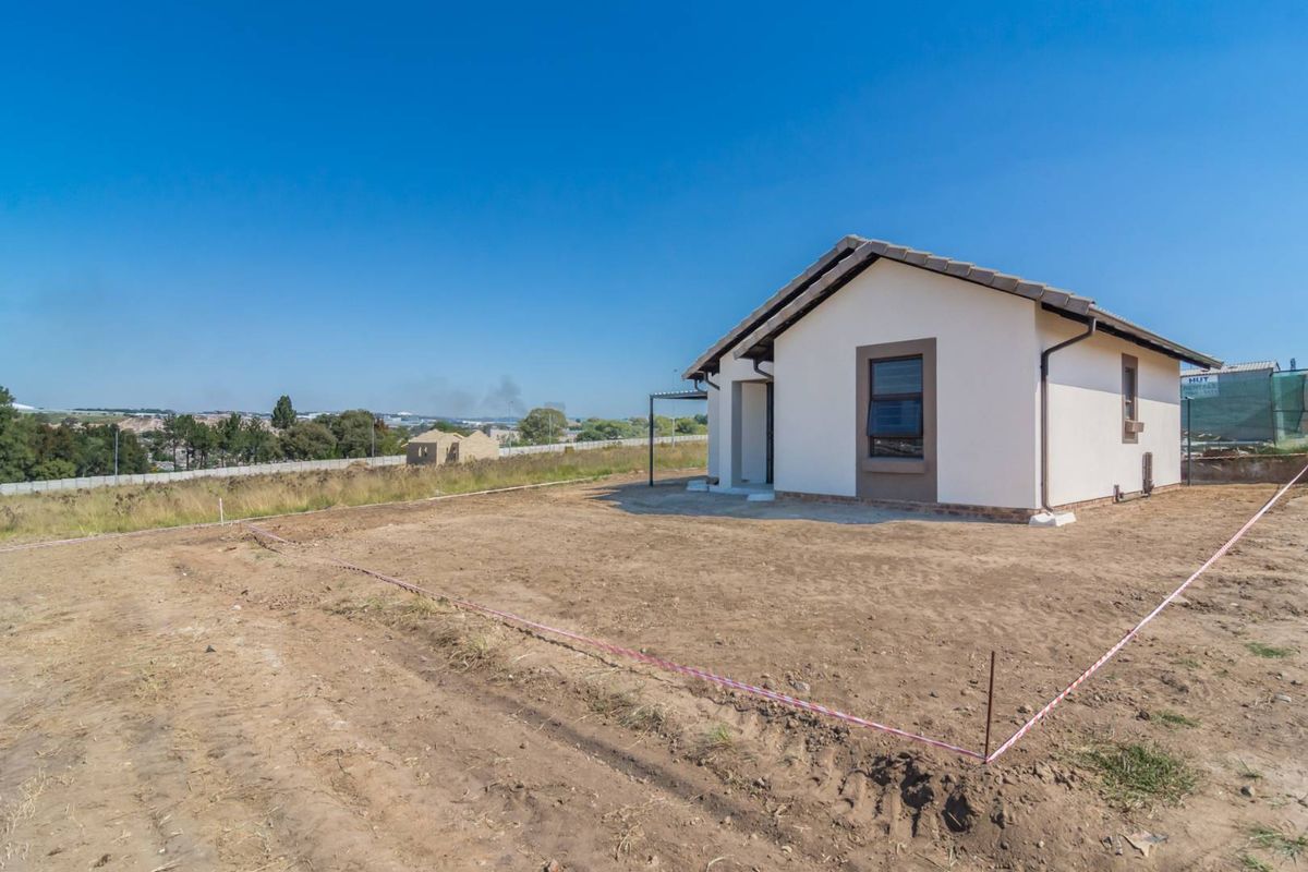 Exterior view of a modern single-story house featuring a tiled roof, neutral facade, and an expansive, undeveloped plot of land.