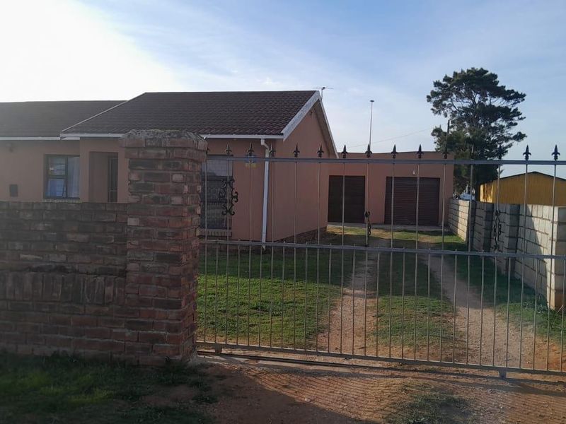 Front view of a single-story house featuring a brick boundary wall, metal gate, and a double garage with a tiled roof.