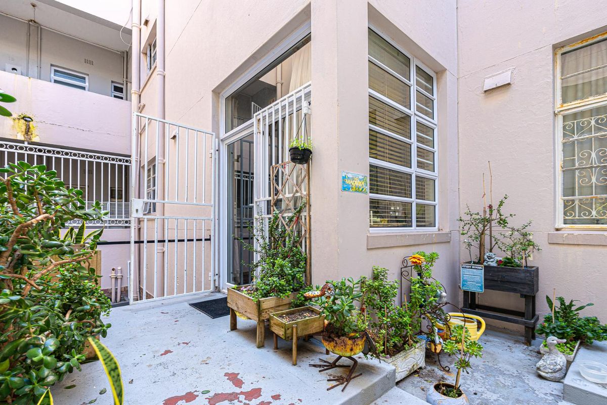 A private rear courtyard area featuring concrete flooring, a security gate, and multi-pane windows providing access to the apartment interior.