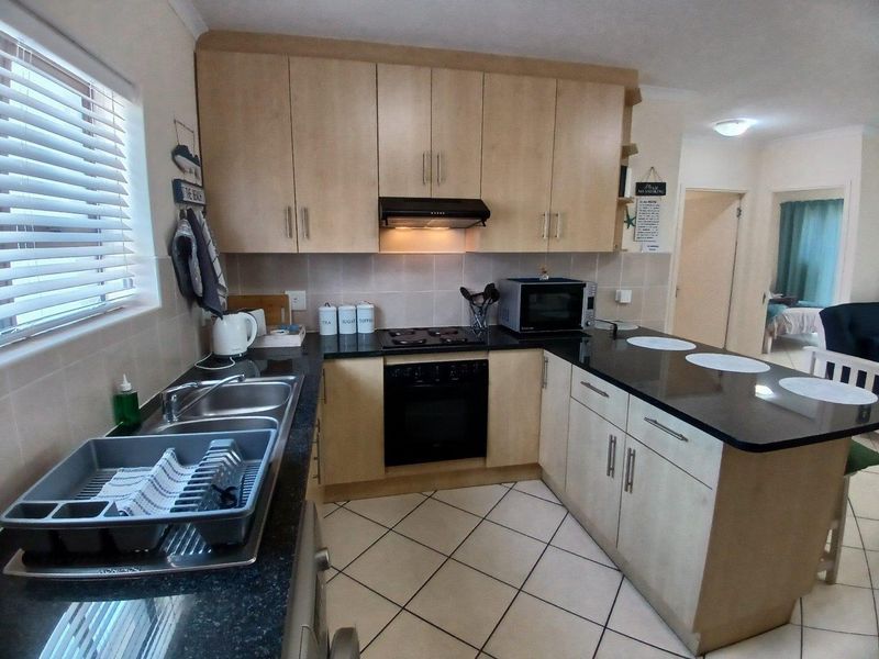 A functional kitchen featuring light wood-tone cabinetry, dark granite countertops, built-in oven, electric hob, and tiled flooring.