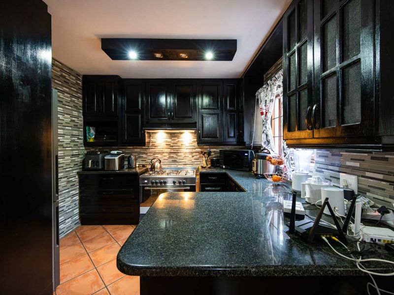 A well-appointed kitchen featuring dark cabinetry, granite countertops, a gas stove, and a decorative tiled backsplash with integrated lighting.
