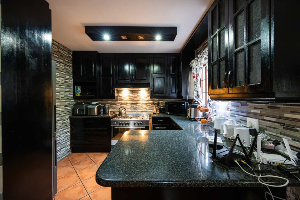 A well-appointed kitchen featuring dark cabinetry, granite countertops, a gas stove, and a decorative tiled backsplash with integrated lighting.