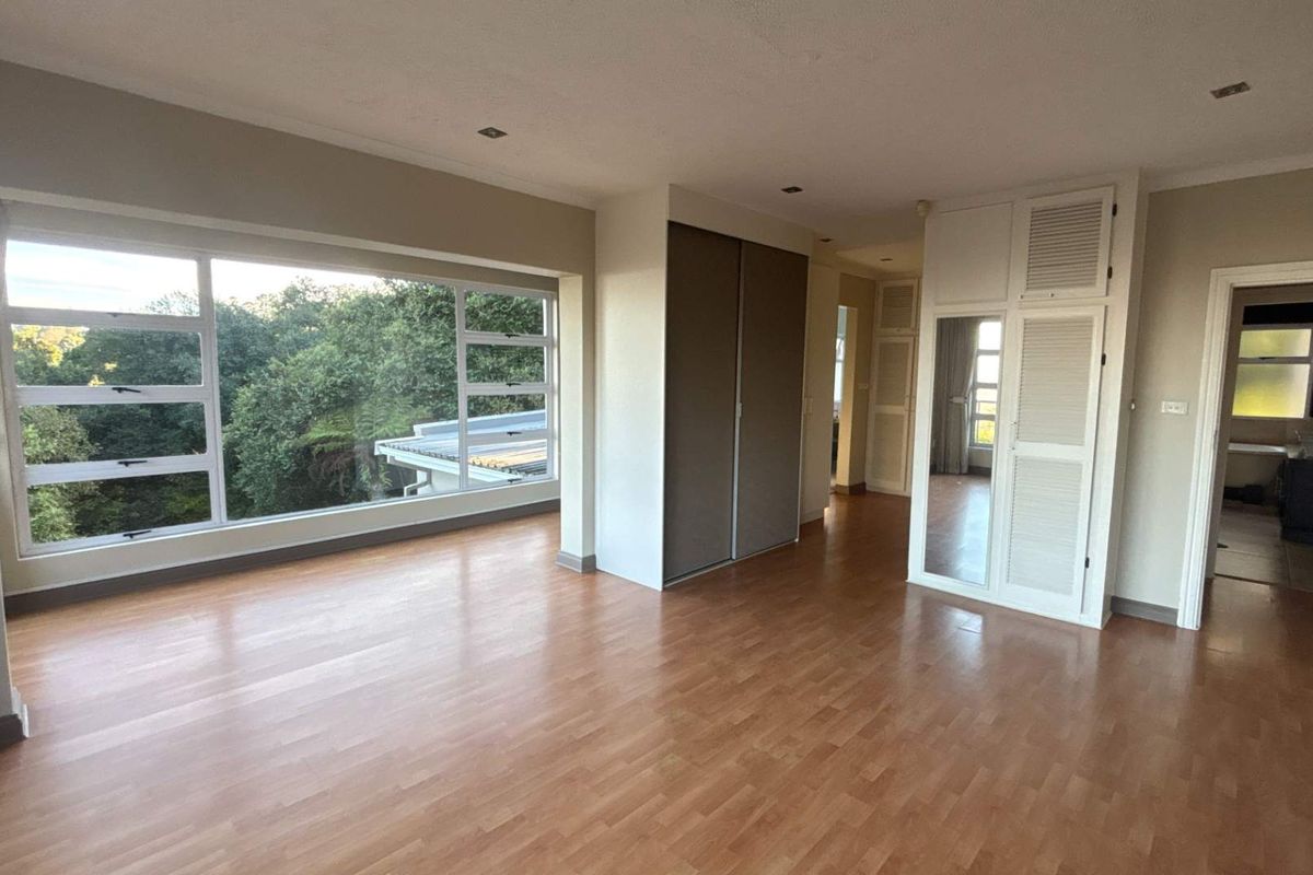 Spacious bedroom featuring large windows with garden views, built-in cupboards, and laminate flooring, leading into an en-suite bathroom.
